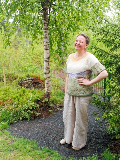 Marja Vanhala seisoo iloisesti hymyillen kesäisen vihreän koivun edessä vasen käsi rennosti vyötäröllä.